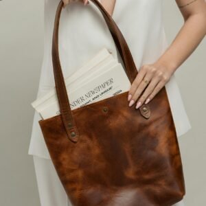 Close-up of a fashionably dressed woman holding a leather tote bag with a newspaper.